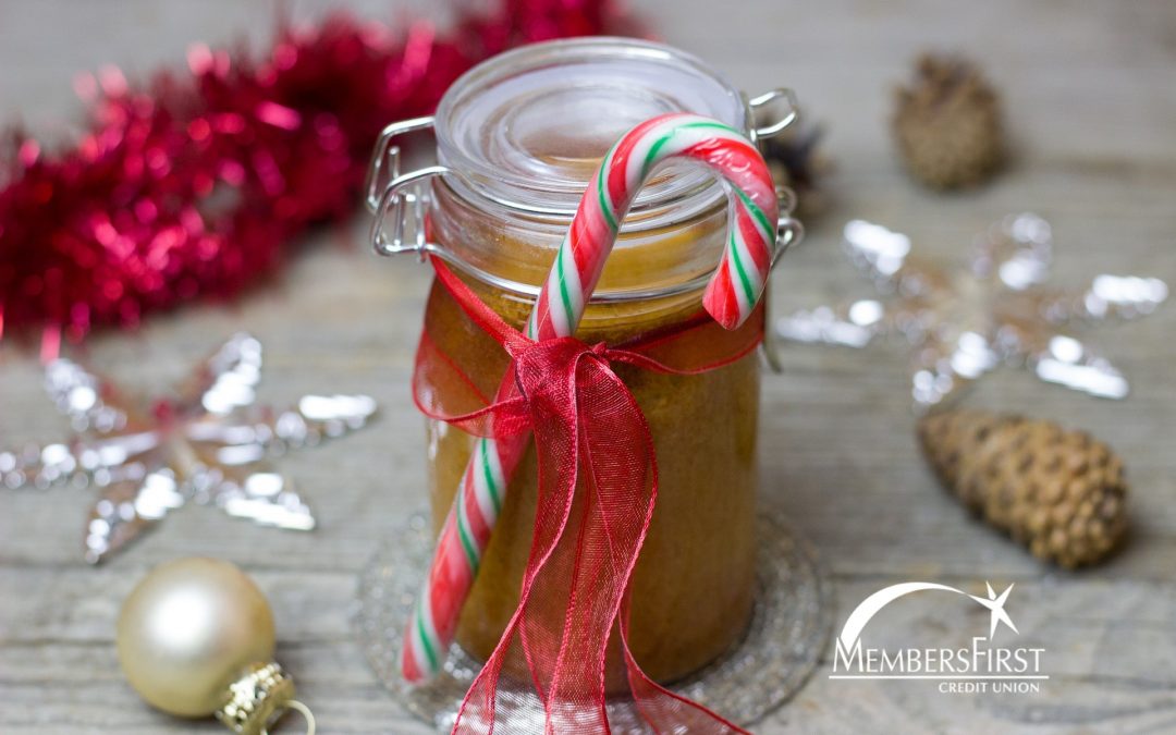 Mason jar with candle cane and ribbon on outside with cake baked inside sitting on table with Christmas ornaments scattered around it.
